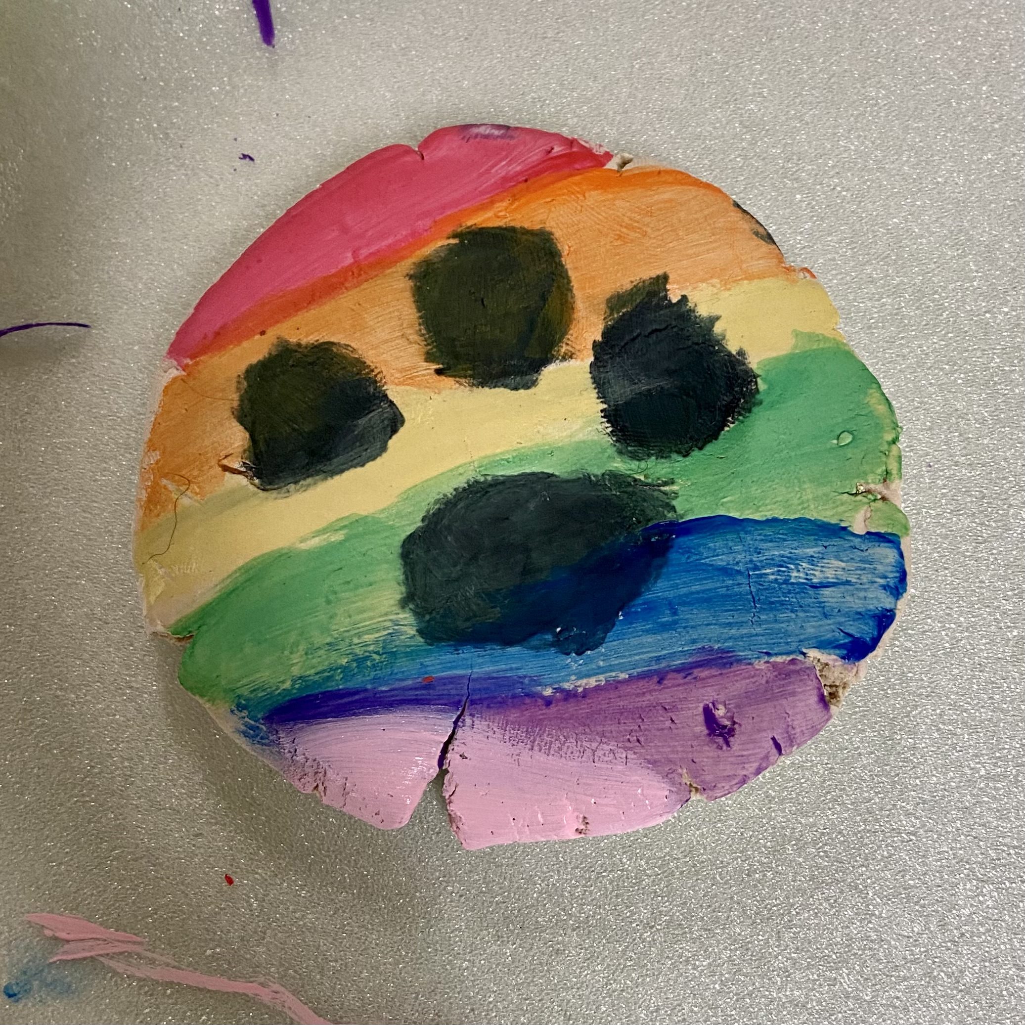 An adorable image of a round Christmas ornament painted with a rainbow and dog paw print by girl scouts.